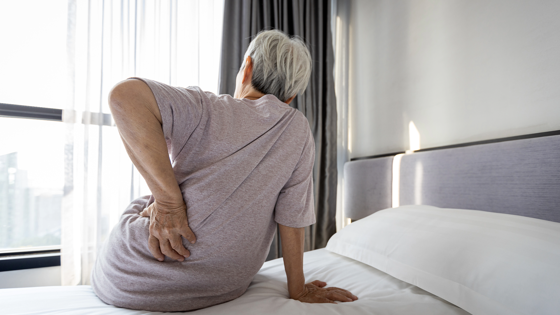 Senior sitting on bed showing discomfort in back