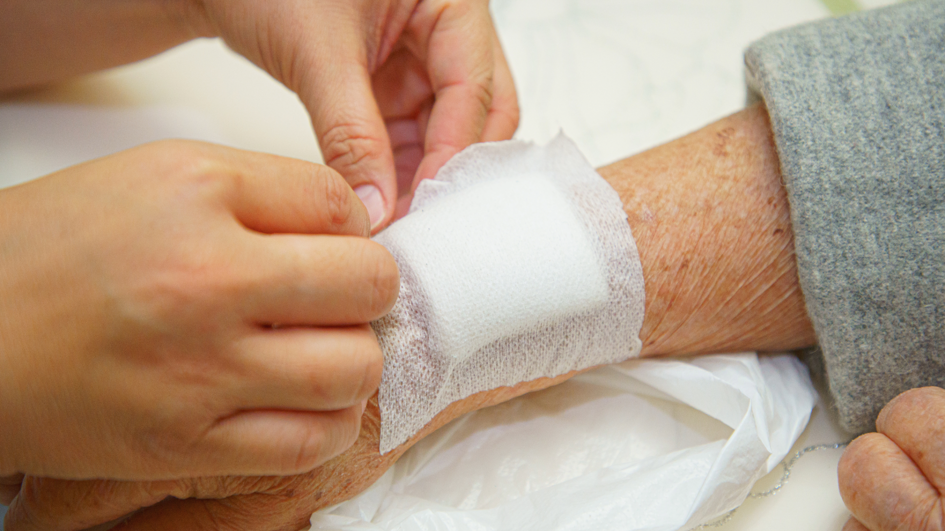 Healthcare professional applying a sterile bandage to an arm of an older adult, illustrating the process of caring for a draining wound.